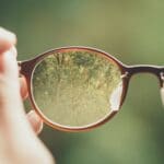 Glasses with a fuzzy green background, but through the glasses lenses detail can be seen