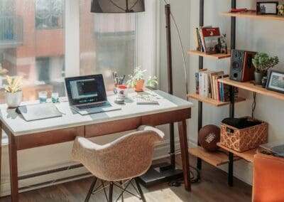 Bedroom showing desk with a laptop and other items, with a stand with speakers, books, photo frames and more