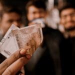 Person holding money (in Indian rupees) with 3 well dressed people in the backgroun side by side ddressed smartly, with a celebration vibe