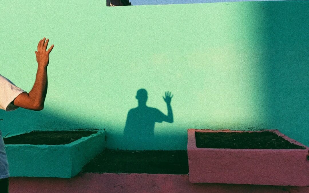 Person waving, can only see their arm and in the background there is a green wall a shadow showing their full torso